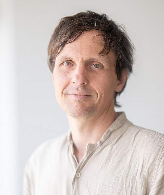 Mann mit beigem Hemd und freundlichem Lächeln